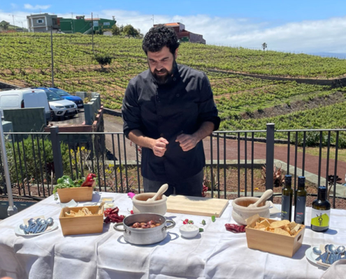 cooking lesson. chef dressed in black at an outdoor table in front of vineyard.